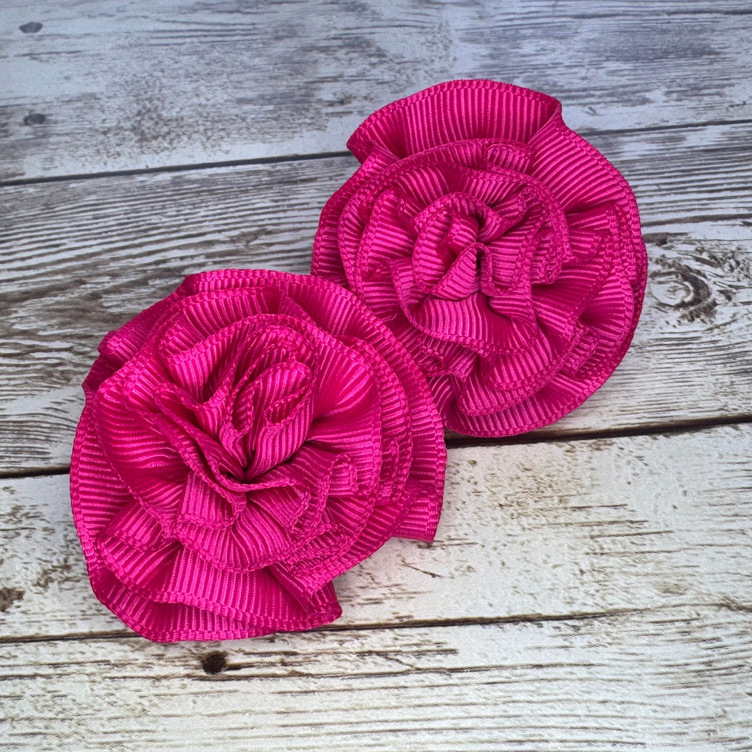 Two pink floral hair clips on a wooden surface
